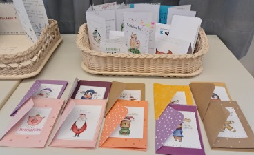 Auf einem Tisch steht ein Korb voller selbst gestalteter Weihnachtskarten. Davor sind weitere zehn bunte Karten ausgelegt.